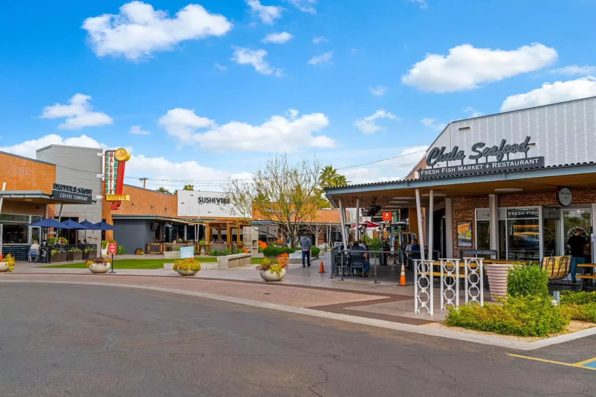 Open-air shopping center with restaurants, planters, and pedestrian walkway.
