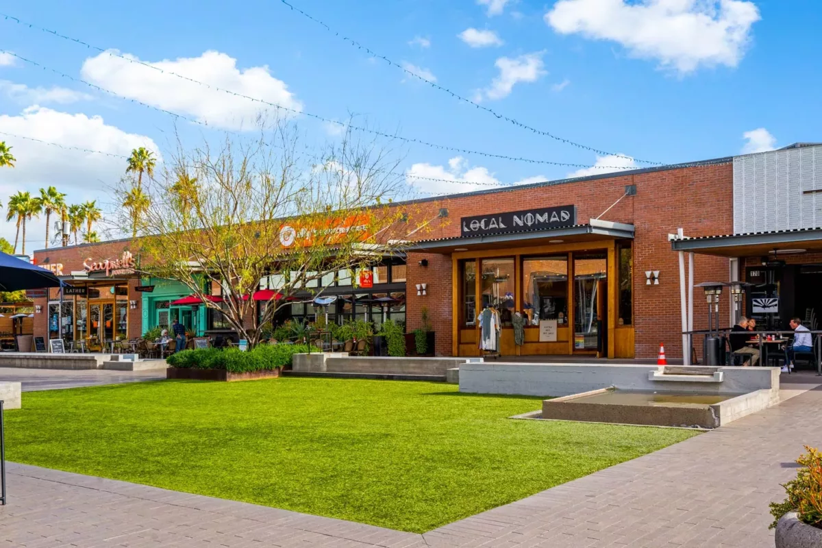 Open-air retail plaza with lawn, storefronts, and outdoor dining patios.