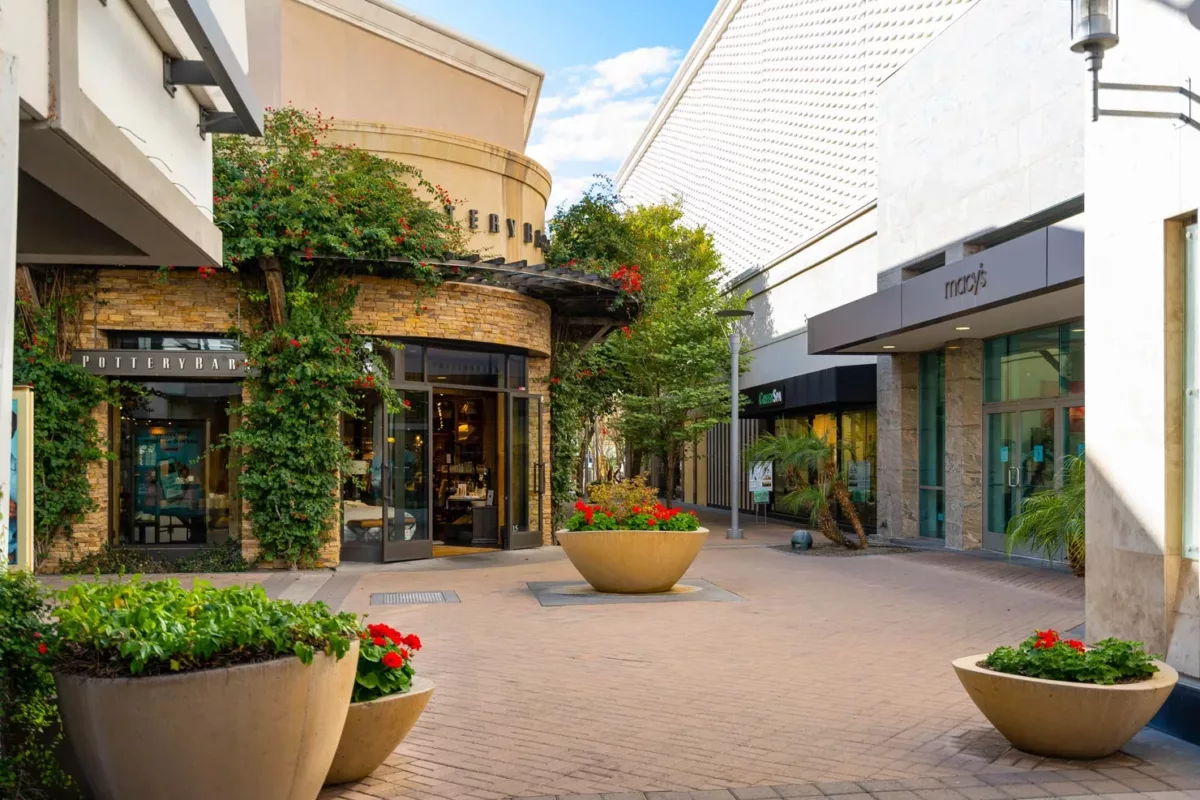Open-air shopping walkway with storefronts, planters, and Macy's entrance.