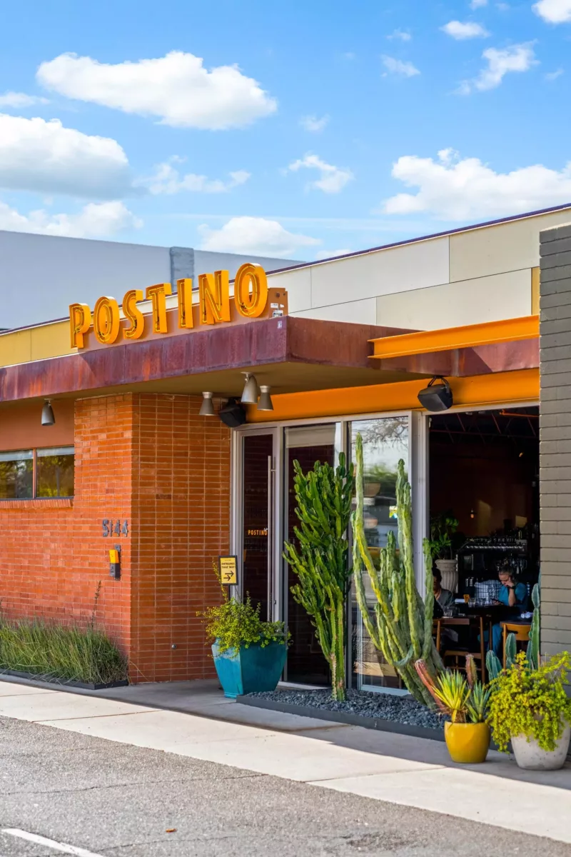 Postino restaurant entrance with orange sign, open doorway, and potted cacti.
