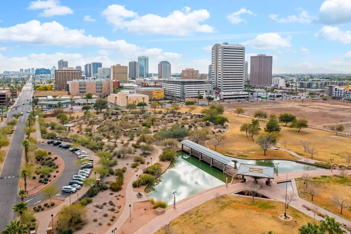 Aerial view of urban park with pond, pathways, and downtown skyline.