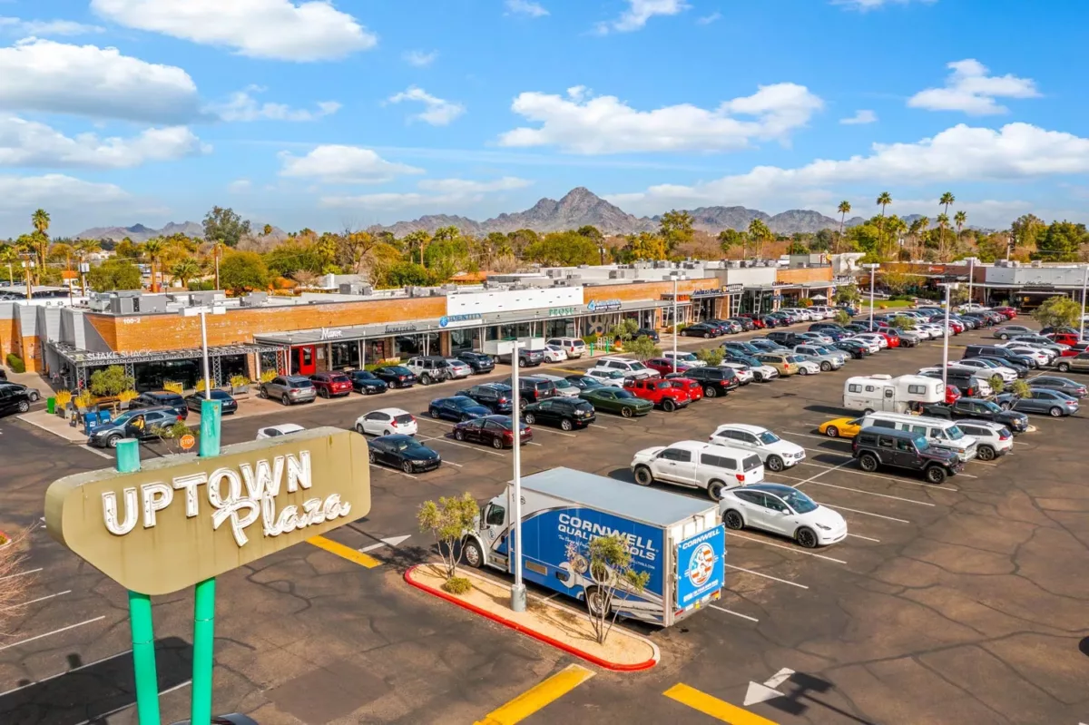 Uptown Plaza shopping center with storefronts, parking lot, and mountain views.